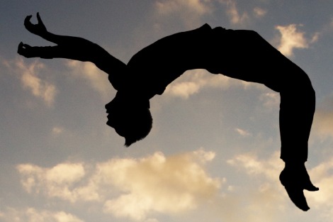 Gymnast performs a backflip, silhouetted against the sky