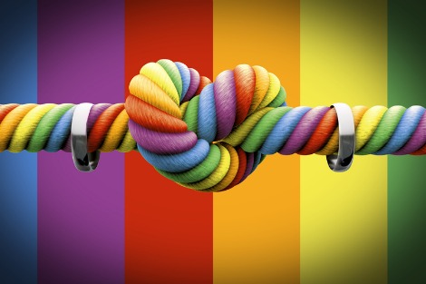Rainbow coloured rope tied in a heart-shaped knot, with a wedding band strung on either side