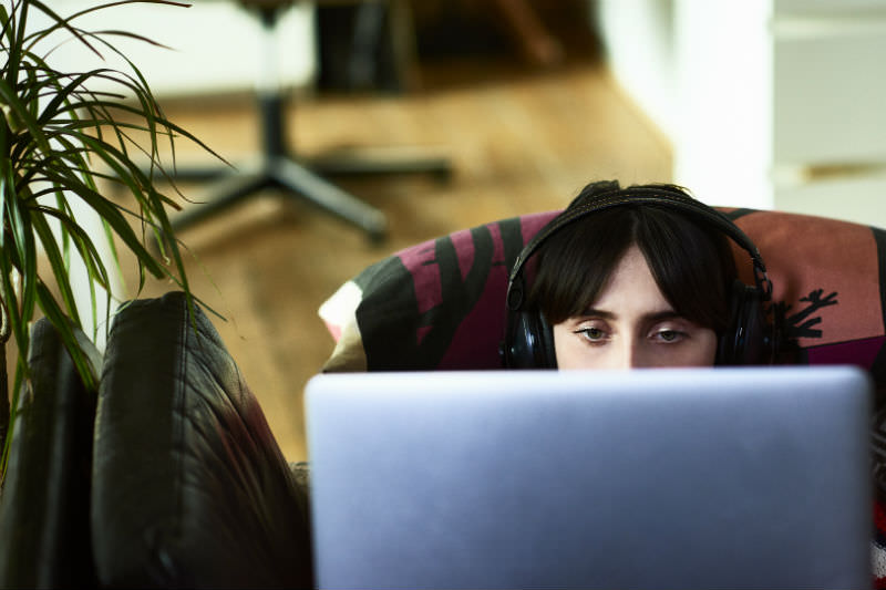 Front view of the top of a young woman's head and eyes as she watches a movie online, relaxing on sofa, listening to music and streaming online content (10'000 Hours / Getty Creative)
