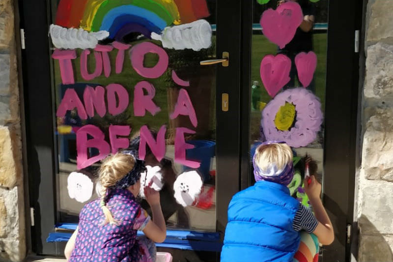 Children drawing on door around the words tutto andra bene (Marta Achler)