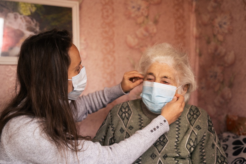 Main image: Main image: Young woman with her grandmother, discussing the coronavirus. Both with protective masks on their face. (Photo by Daniel Balakov/Getty Images)