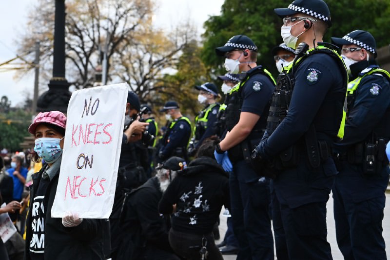 Woman holds poster 'No knees on necks' while police stand in background  (Photo by Quinn Rooney/Getty Images)