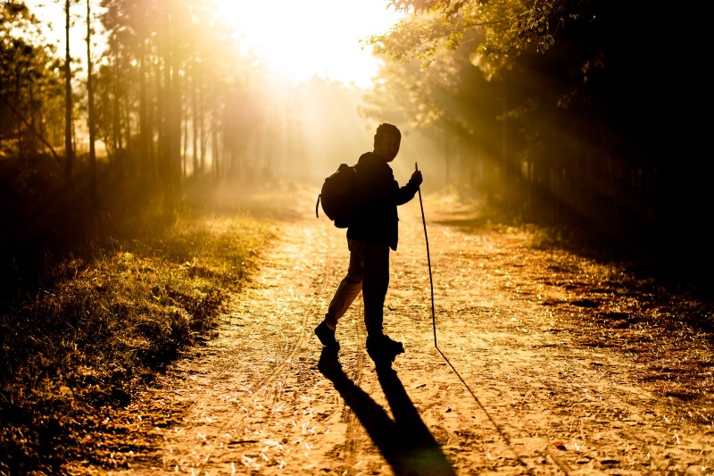Silhouette of man walking on road holding stick (Autthaporn Pradidpong/Unsplash)