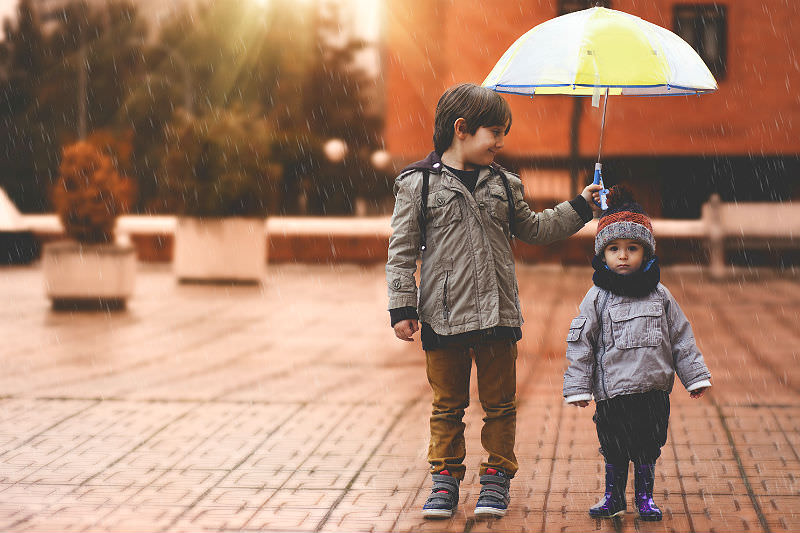 A little boy and his older brother protect themselves from the rain with an umbrella. (Estersinhache fotografía / Getty)