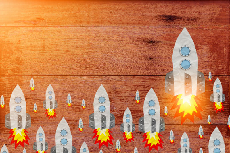 Rocket paper-cut shape on old wood plank with rustic texture background. Credit: whyframestudio / Getty