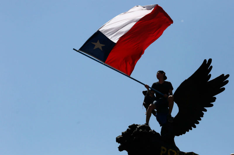A demonstrator waves a Chilean flag atop a monument (Getty images/Marcelo Hernandez)